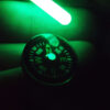 Small glow stick from the Mini Survival Tin illuminating the button compass for navigation in the dark.