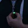 A Glo Zip zipper pull glowing with a green glow-in-the-dark effect, attached to a jacket zip as a tactile zip pull extension and personal marker.