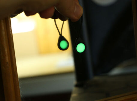 A Glo Zip zipper pull glowing with a green glow-in-the-dark effect, being held up to mirror to show its double-sidedness.