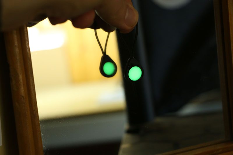 A Glo Zip zipper pull glowing with a green glow-in-the-dark effect, being held up to mirror to show its double-sidedness.