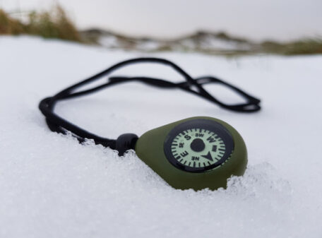 The CMP-20 Compass Necklace on snowy ground, with the oil-filled dial working perfectly as it won't freeze in sub-zero conditions.