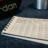 The Pocket Gym Diary with a workout recorded, next to a dumbbell and sports drink bottle.