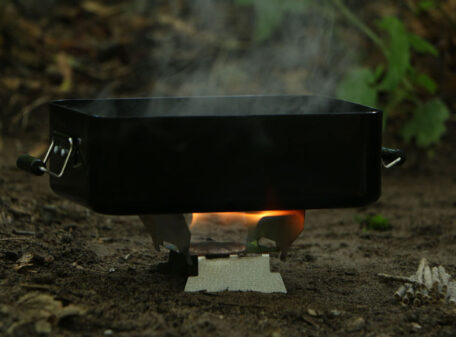A lightweight emergency folding camping stove set up on a hike in the woods, burning some Exogel Camping Stove Gel Fuel, to boil a mess tin full of water.