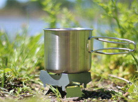 The Emergency Stove being used by a lake in the wilds, boiling some water in a camping pot.