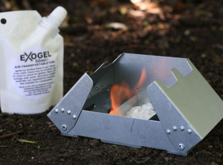 A lightweight military folding camping stove set up on a hike in the woods, burning some Exogel Camping Stove Gel Fuel.