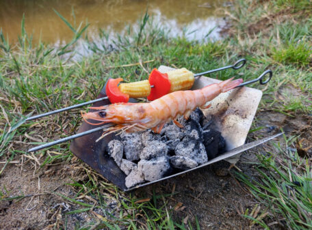 The Stealth Stove burning some charcoal being used with the wider base at the top as a mini barbecue with prawn and vegetable skewers cooking on top.