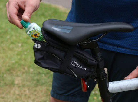 The Green Machine thin-film chain lube bottle being placed into a small saddle bag on a bicycle.