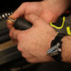 The MagModule is strapped to a man's wrist, with some screws and a screwdriver bit attached to the magnet, while the man is changing the bit in a cordless drill / driver.