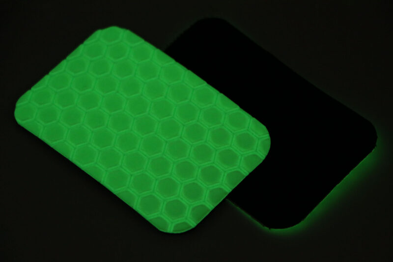 Two Cyflect Patches laying back to back, glowing in the dark with a bright green glow.