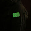 The glowing Cyflect Patch, attached to shoulder of a military jacket.