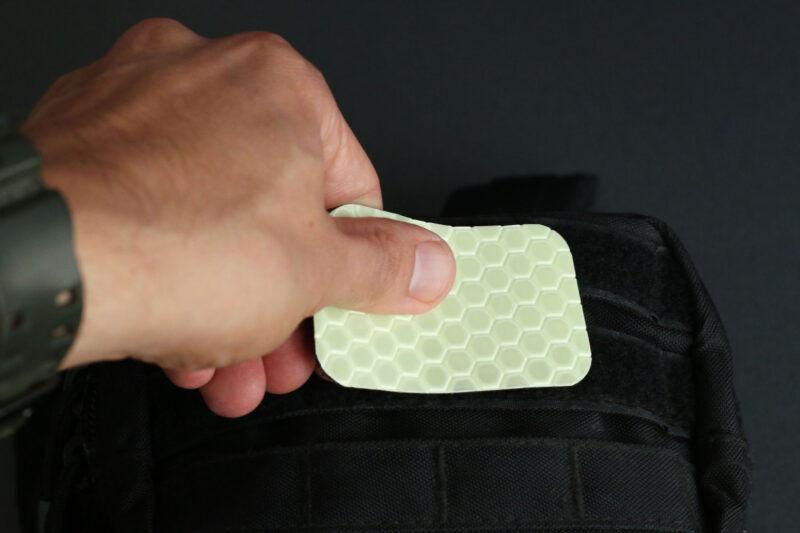 Applying the Cyflect Patch to a tactical black rucksack, using the hook and loop attachment.