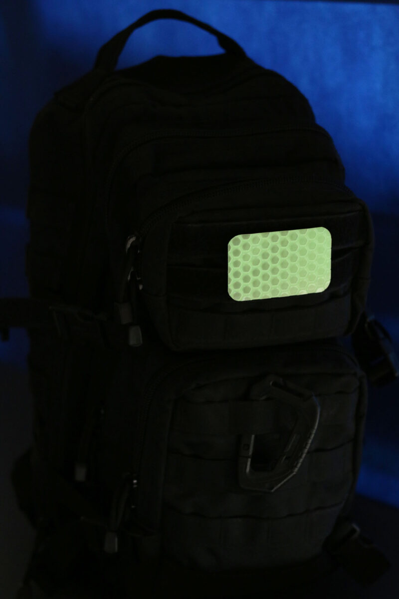 The glowing Cyflect Patch, attached to a tactical black rucksack.