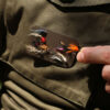 The Mag Patch affixed with hook and loop to a fishing jacket, with a selection of fish hooks and trout fly lures magnetically attached.