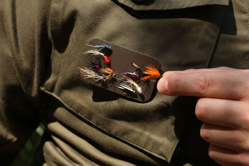 The Mag Patch affixed with hook and loop to a fishing jacket, with a selection of fish hooks and trout fly lures magnetically attached.