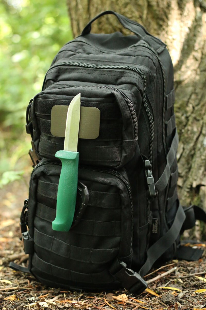 The Mag Patch affixed with hook and loop to a tactical rucksack, with a bushcraft knife magnetically attached during a woodland camp.