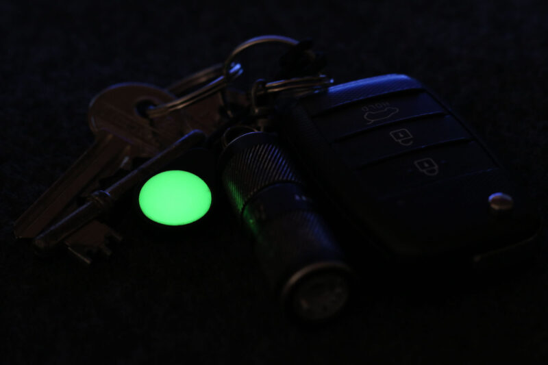 A Magnetag attached to a bunch of keys, glowing bright green in the dark as a gear marker.