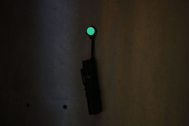 A Magnetag, being used to hang a flashlight from a steel surface, while the glow-in-the-dark element glows bright green as a gear marker.
